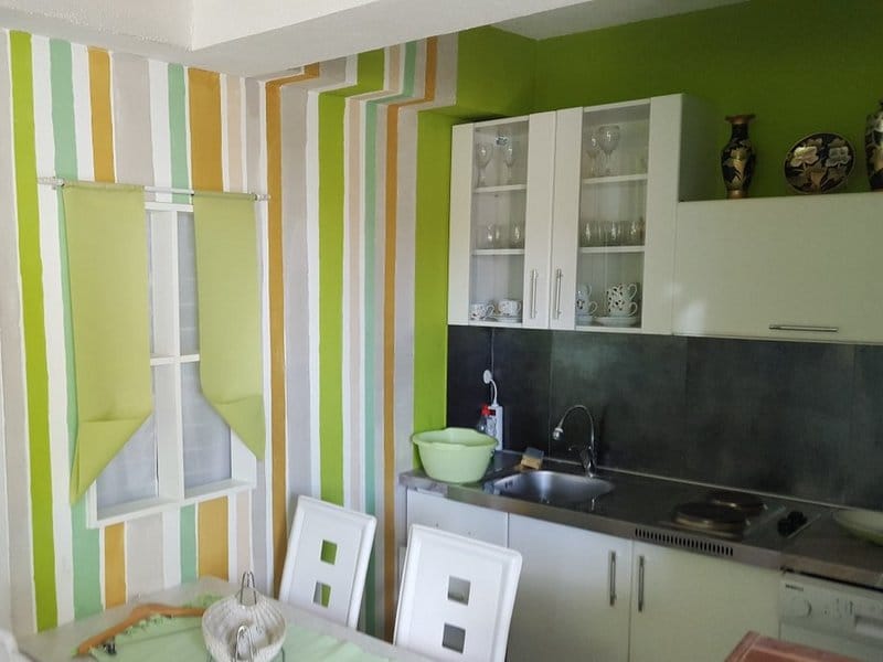 Kitchen in a house in Krimovica, Montenegro: white furniture, striped green-toned walls, and a dining area.