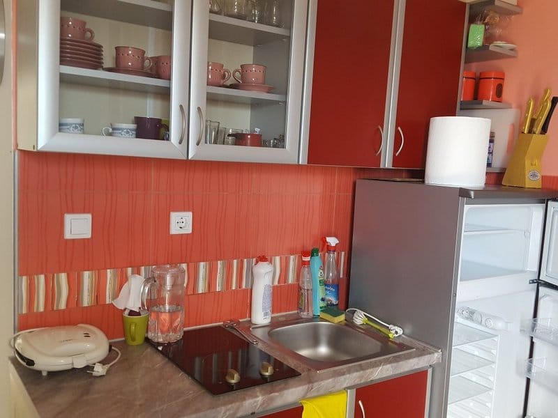 Compact kitchen with red cabinet fronts, a stove, and a refrigerator in a house for sale in Krymovice, Montenegro.