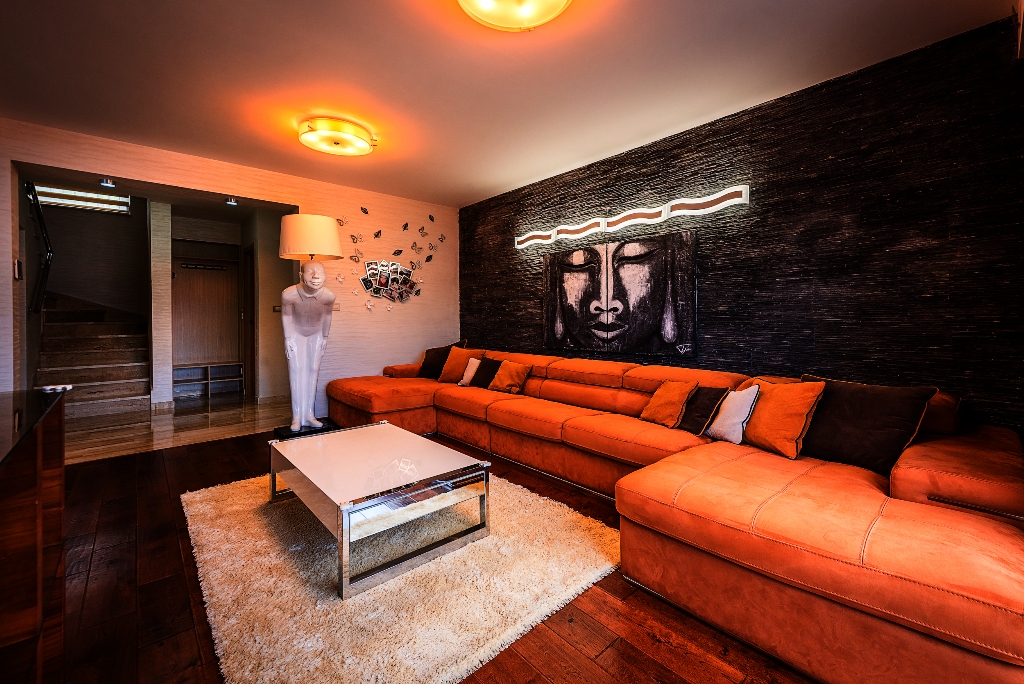 Living room of a villa in Krašići, Montenegro: orange corner sofa, stone accent wall, and designer floor lamp.