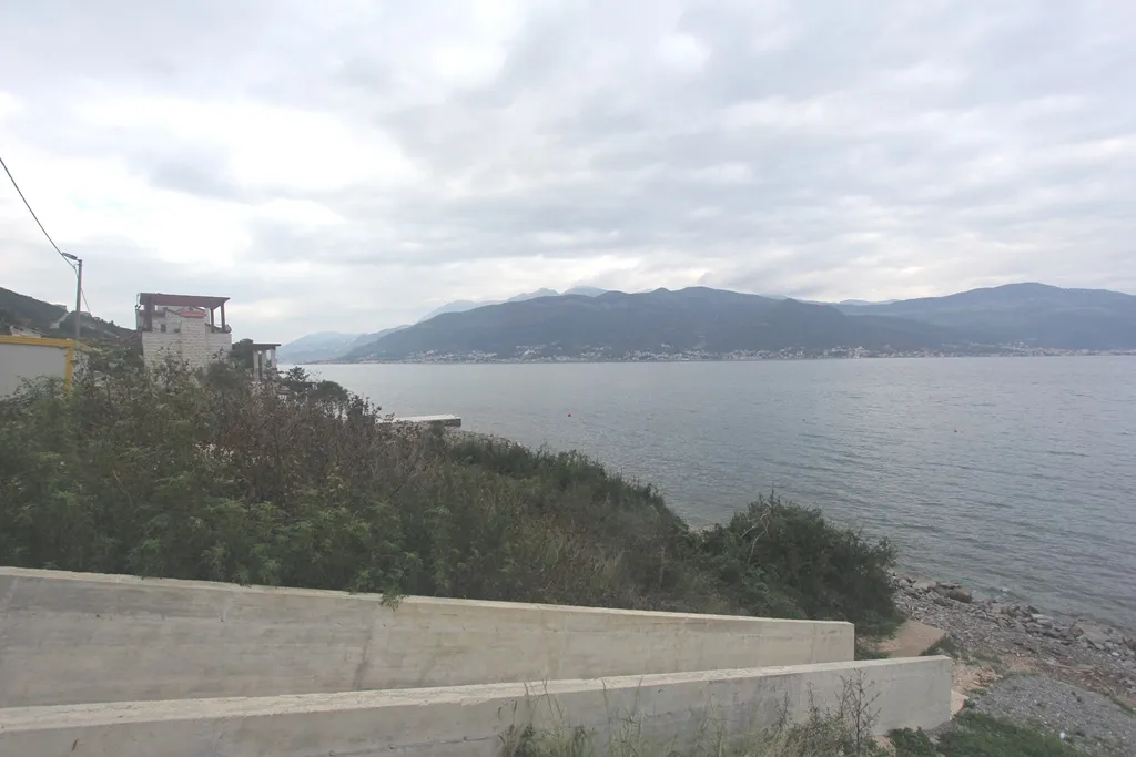 View of water and mountains from the shore, showing concrete retaining walls and vegetation.
