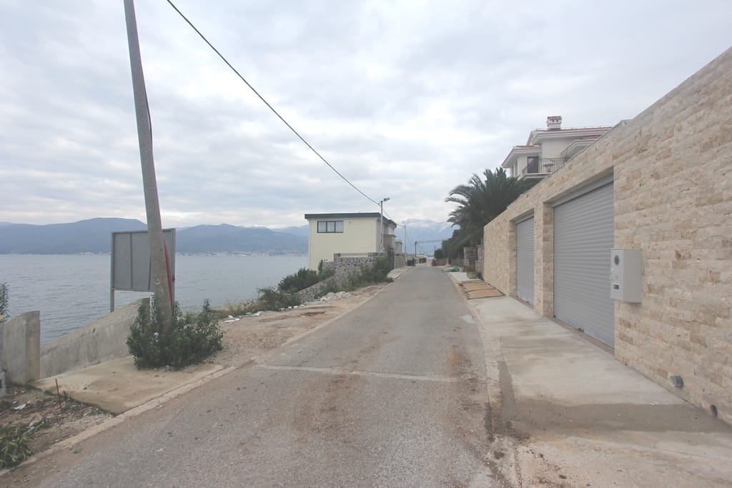 Land plot in Krašići, Montenegro: view of the coastal road, stone fence, and sea landscape with mountains.