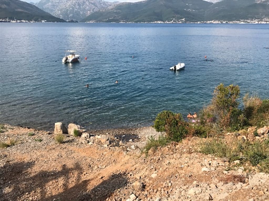 Sea and mountain view from a land plot in Krašići, Montenegro: private beach, boats, and panoramic sea landscape.