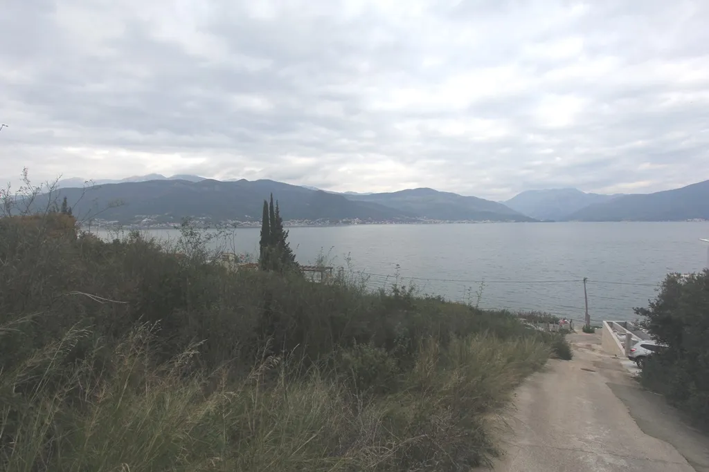 Scenic view of the sea and mountains from overgrown land with a dirt road.