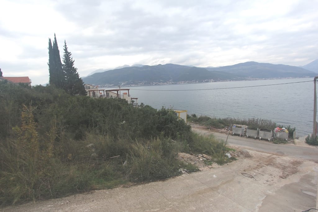 Land plot in Krašići, Montenegro: panoramic view of the sea, mountains, and coastal road with cypress trees.