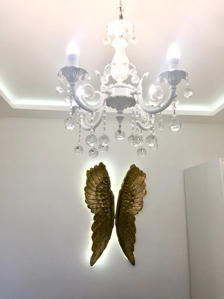 White crystal chandelier and golden wings on a wall; only ceiling and decor are visible.