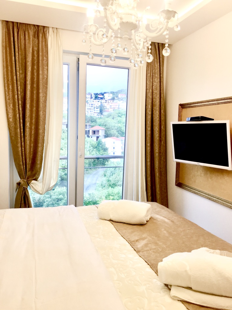 Cozy bedroom in an apartment in Bečići, Montenegro: double bed, TV, crystal chandelier, and mountain view.
