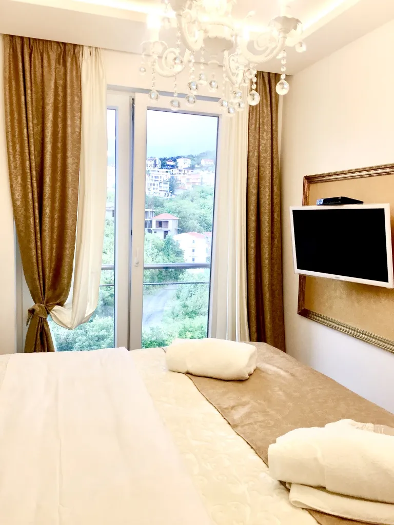 Bedroom featuring a large bed with white towels, crystal chandelier, and TV near the window.