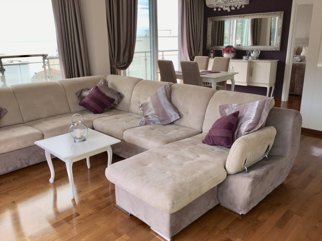 Living room with a beige corner sofa and sea view in an apartment in Becici, Montenegro. Interior with dining area.
