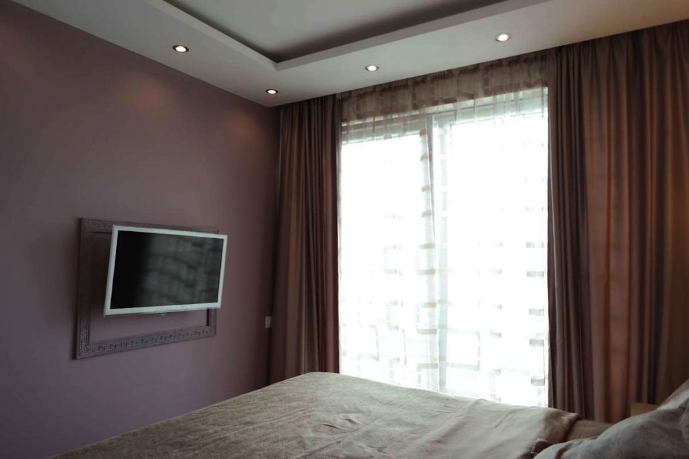 Bedroom in an apartment in Becici, Montenegro: double bed, wall-mounted TV, panoramic window with blackout curtains.