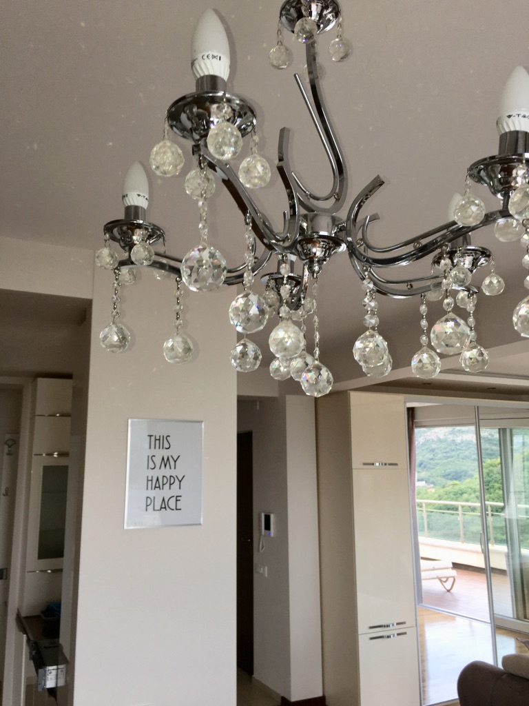 Crystal chandelier in a modern apartment living room in Bečići, Montenegro, with a view of the terrace and mountains.