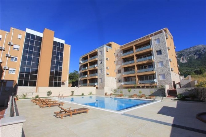 Modern residential complex with a pool and sun loungers in Bečići, Montenegro: view of the building facade and relaxation area.