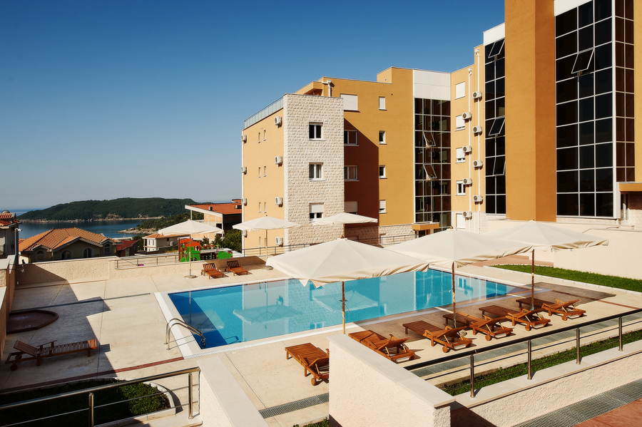 Outdoor pool with sun loungers at a residential complex in Bečići, Montenegro, with panoramic sea and mountain views.