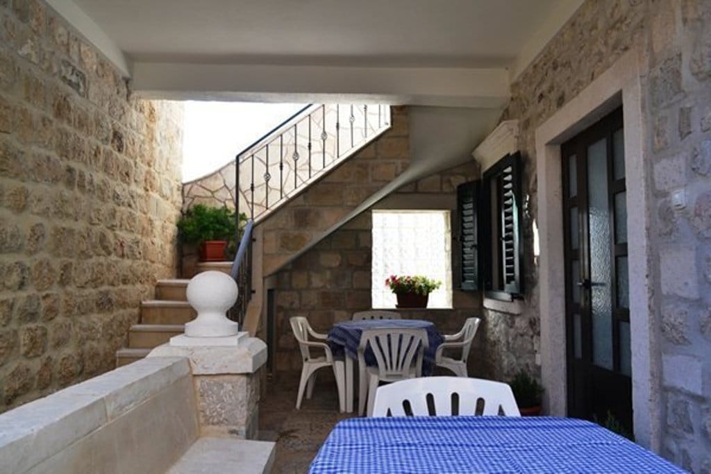 Cozy terrace of a stone villa in Prčanj, Montenegro: tables with chairs, wrought-iron staircase, and traditional finishes.