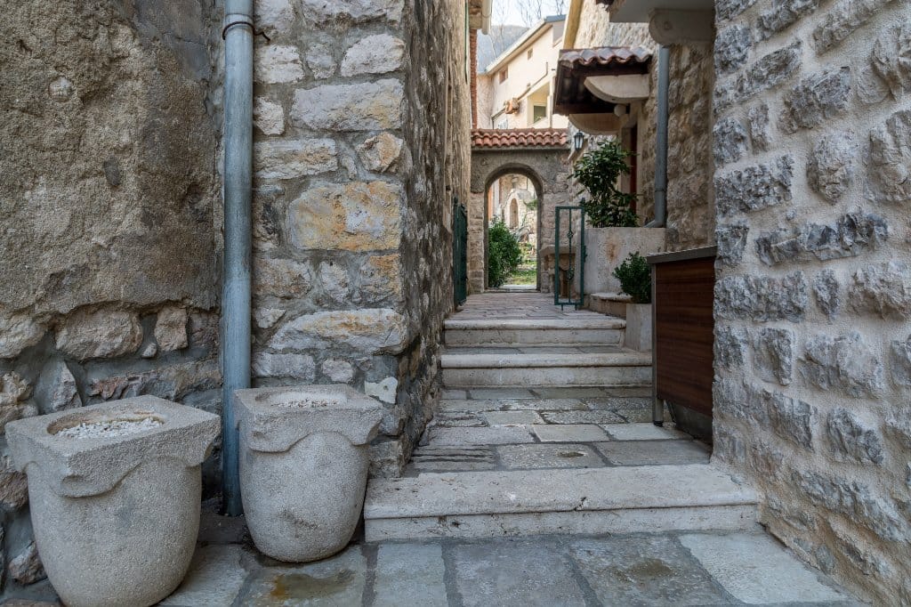 A narrow stone alley with stairs and antique planters by a villa in Prčanj, Montenegro.