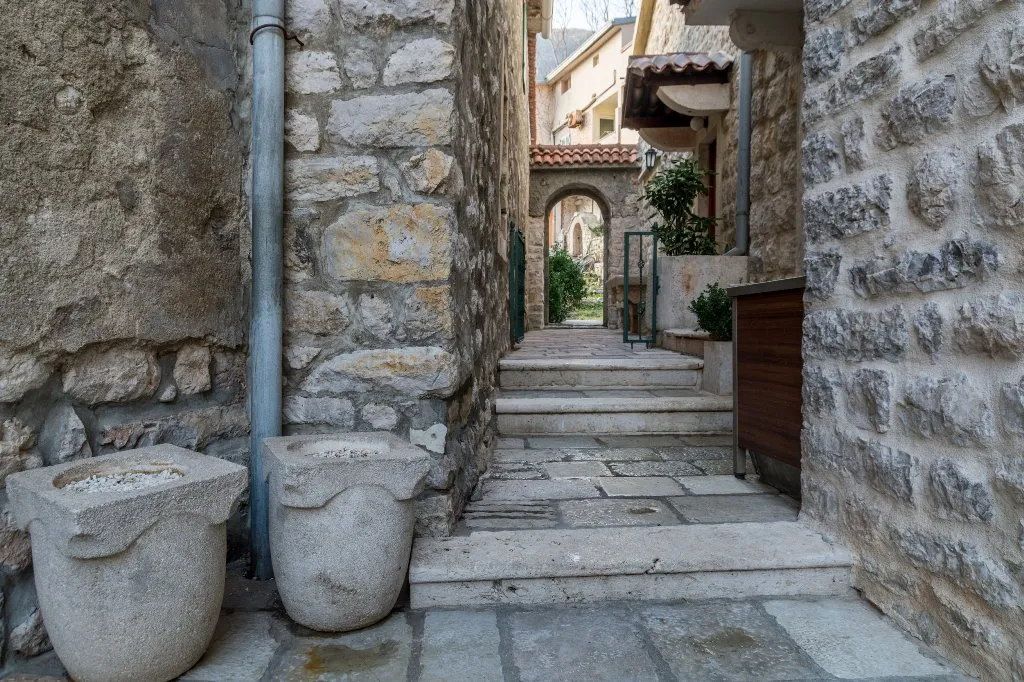 Stone alleyway with steps, ancient stone pots, and an archway leading to another building.