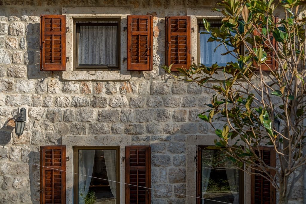 Facade of a villa made of natural stone with wooden shutters in Prčanj, Montenegro, exterior view of the building.