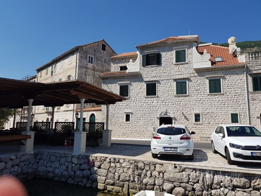 Traditional stone villa in Prčanj, Montenegro, with a terrace by the sea and parked cars in front of the building.
