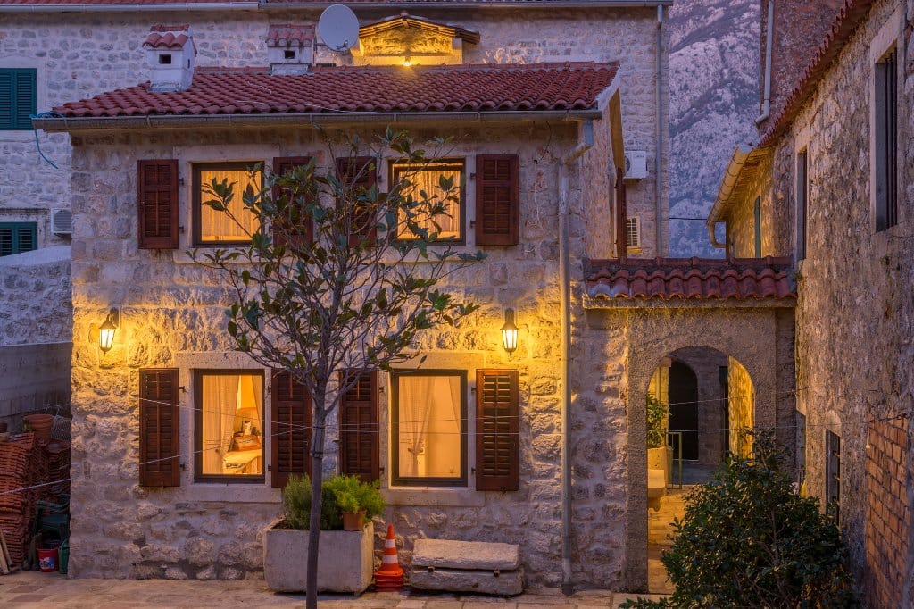 Evening facade of a stone villa in Prčanj, Montenegro: traditional architecture, tiled roof, and cozy lighting.