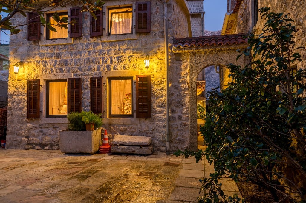 Facade of a stone villa in Prčanj, Montenegro: traditional architecture, cozy lighting, and a stone-paved courtyard.