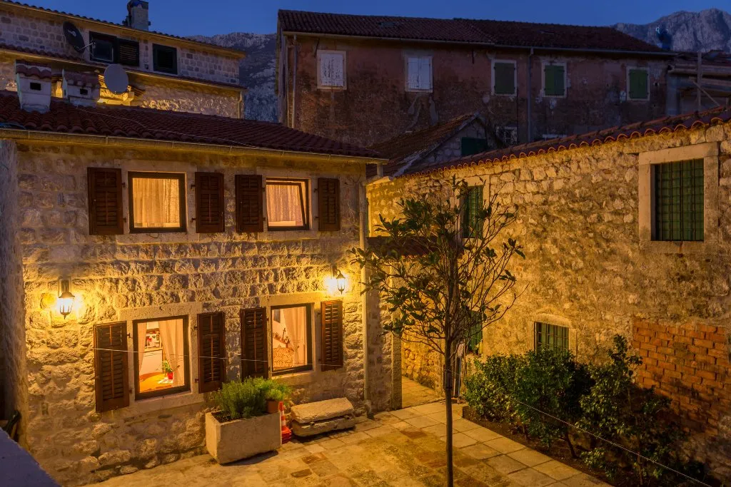 View of a stone courtyard and building facades with lit windows at dusk.