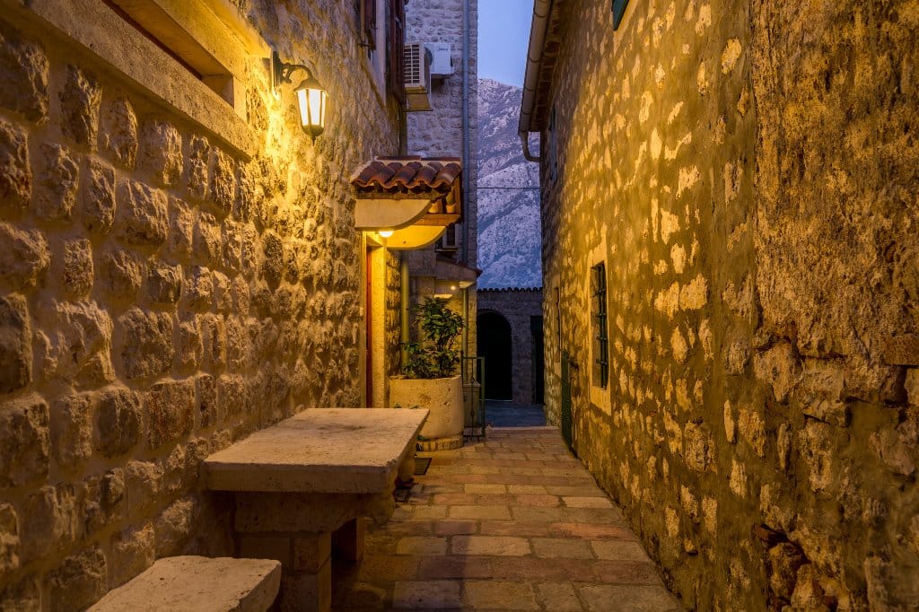 Cozy villa courtyard in Prčanj, Montenegro: stone walls, an antique table, and mountain views in the evening light.