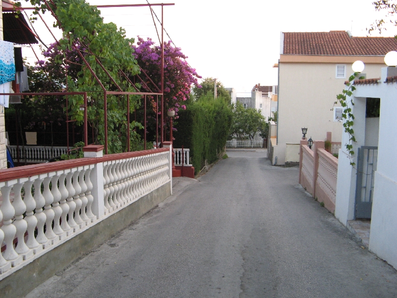 Cozy street with flowering plants by the house in Shushan, Montenegro: view of the driveway and balustrade fence.