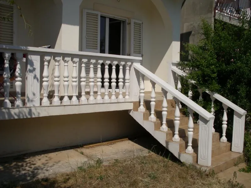 White balcony with decorative balusters and stairs leading to an open door with louvered shutters.