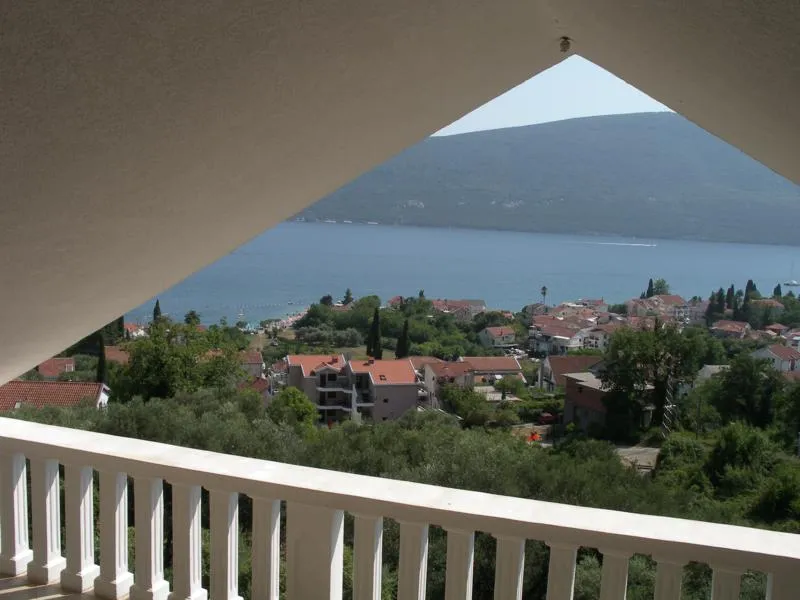 View from a balcony overlooking the sea and town, featuring a white railing and triangular overhang.