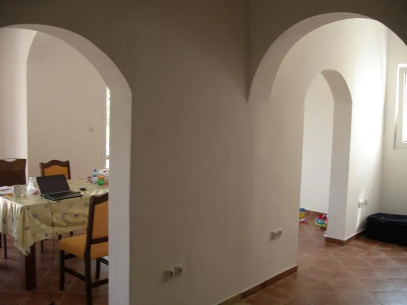 Interior with arched doorways showing a dining area with a table, laptop, and chairs on terracotta tiles.