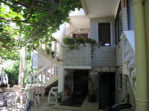 Cozy house terrace in Bečići, Montenegro, with a grape arbor, stone staircase, and a garden seating area.