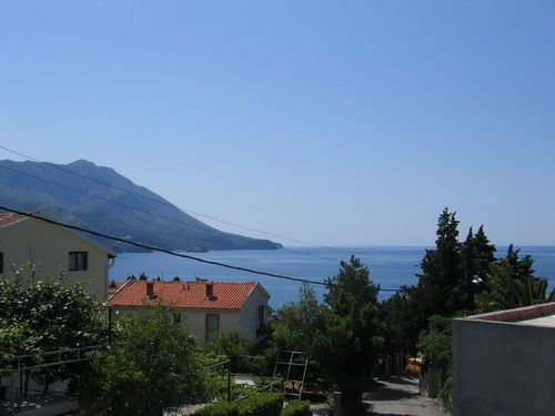 Panoramic sea and mountain view from a house in Bečići, Montenegro: tiled roofs, greenery, and a seascape.