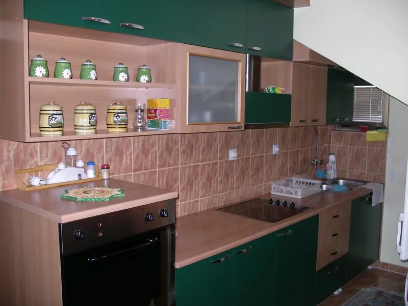 Kitchen with green and wood cabinets, stove, oven, sink, and shelves holding decorative jars.