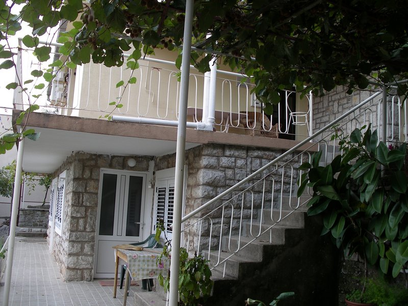 Two-story house in Petrovac, Montenegro: stone facade, open terrace, and staircase in a green garden.