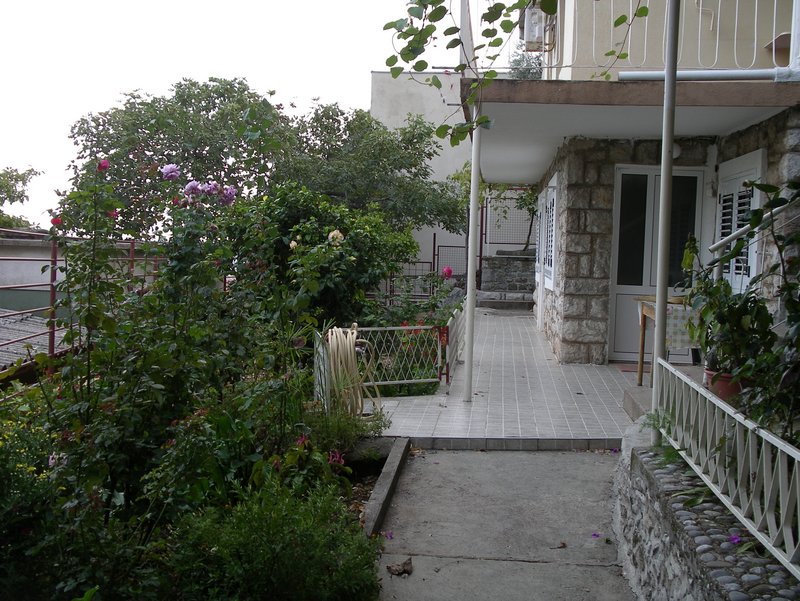 Cozy terrace and blooming garden by the house in Petrovac, Montenegro: stone facade finish and view of the yard area.