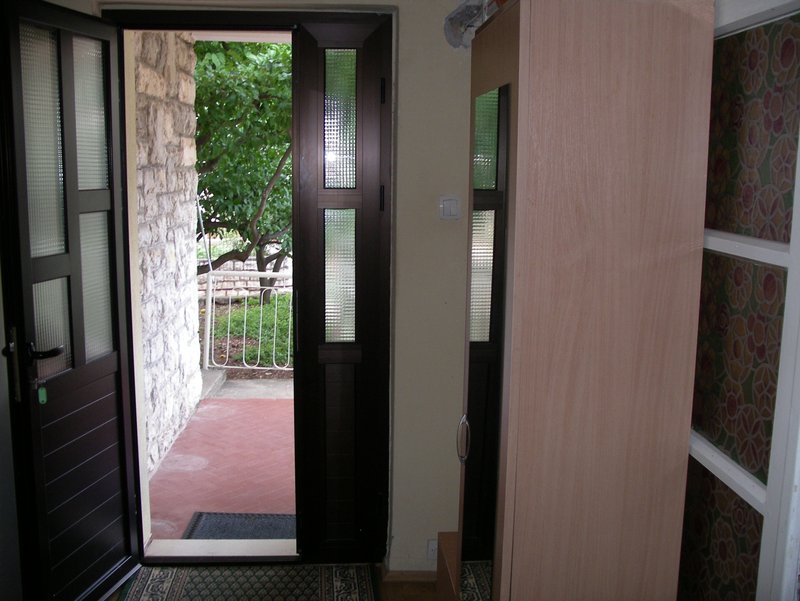 Entrance to a house in Petrovac, Montenegro: an open door to the terrace with stonework, a light-colored cabinet, and a view of the garden.