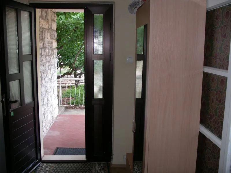 Entryway with open dark door leading to a patio with a stone wall and greenery outside.