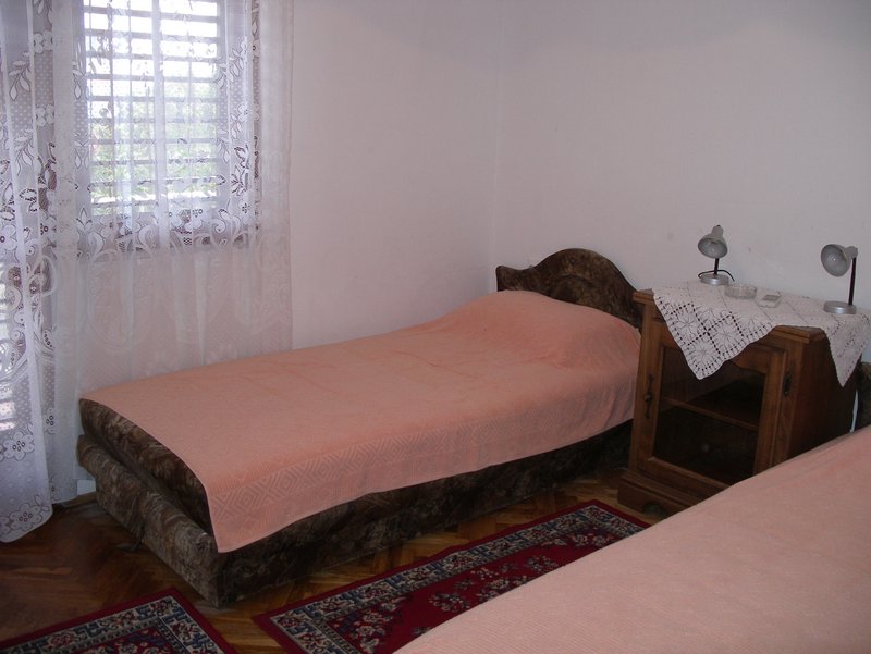 Bedroom in a house in Petrovac, Montenegro: a single bed, a wooden nightstand, parquet flooring, and rugs on the floor.
