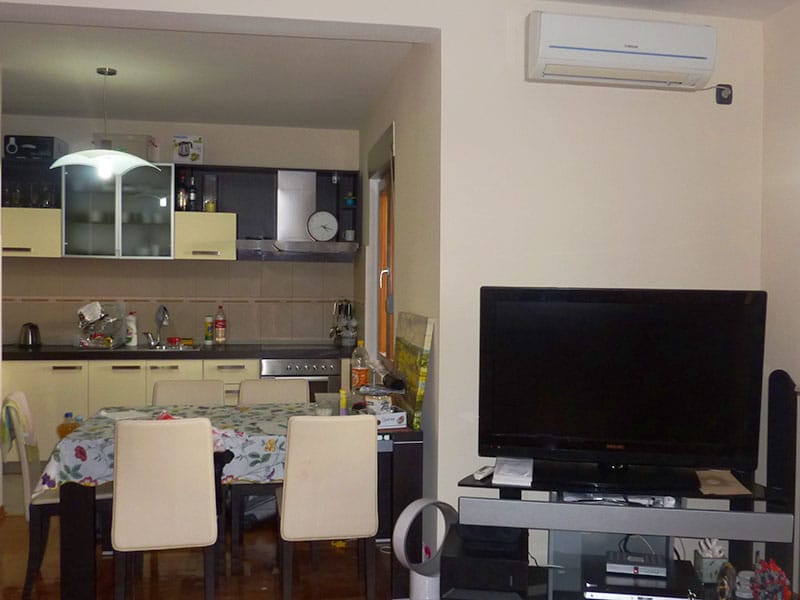 Living room with kitchen and dining area in an apartment, Sveti Stefan, Montenegro: light-colored furniture, TV, and air conditioner.
