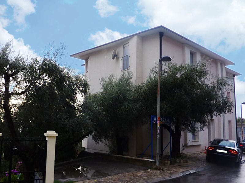 Three-story residential house in Sveti Stefan, Montenegro, with olive trees and parking in front of the building.