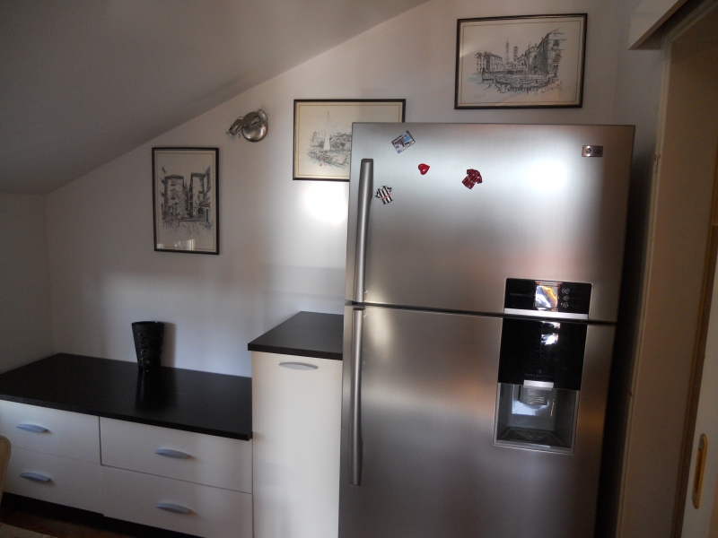 Modern kitchen in an apartment in Budva, Montenegro: LG refrigerator, white cabinets with a black countertop, and wall decor.