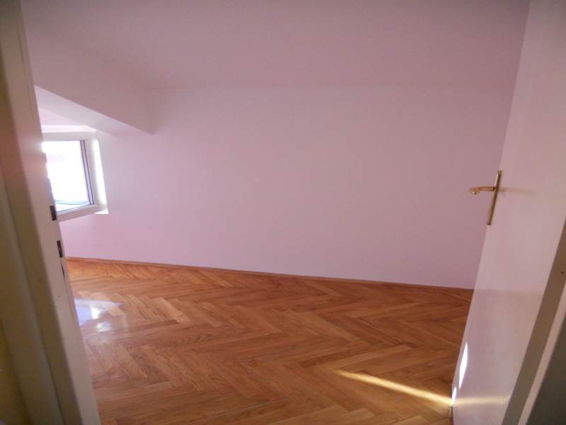 Bright empty bedroom with parquet flooring and a window in an apartment for sale in Budva, Montenegro.