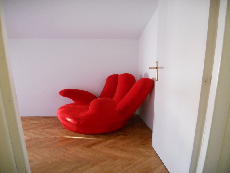 Bright red designer armchair in the living room of an apartment in Budva, Montenegro, with parquet flooring and white walls.