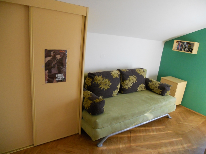 Living room in an apartment in Budva, Montenegro: floral-print sofa, sliding wardrobe, parquet flooring, and a green accent wall.