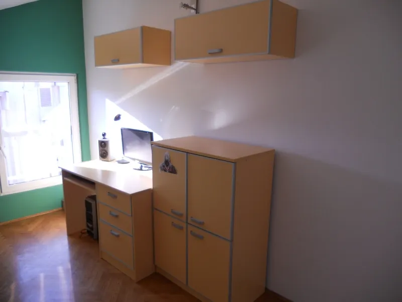 Комната с рабочим столом, компьютером и светлыми шкафами на паркетном полу у окна.
