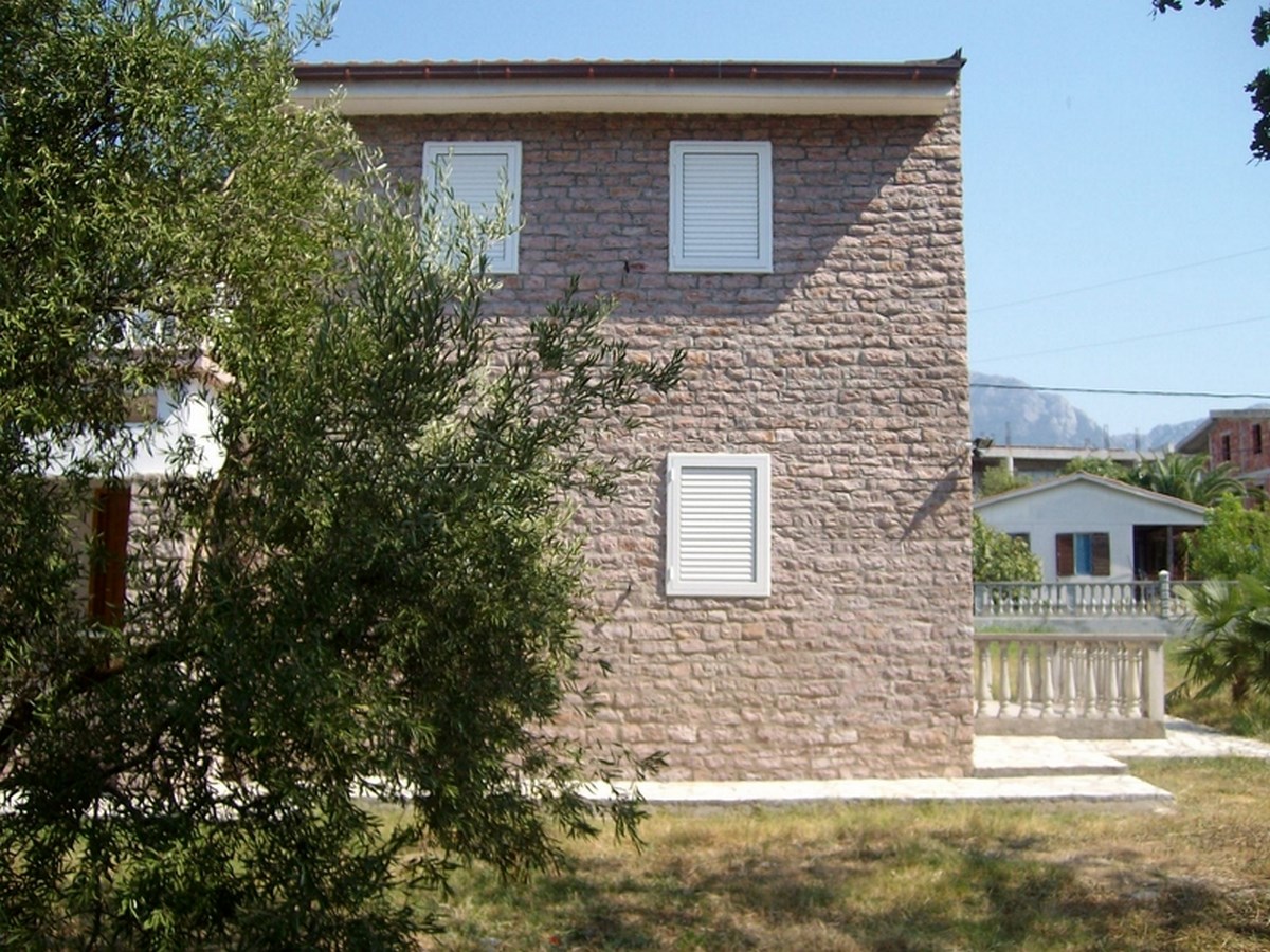 Two-story natural stone villa with white shutters in Bar, Montenegro, front and garden view.