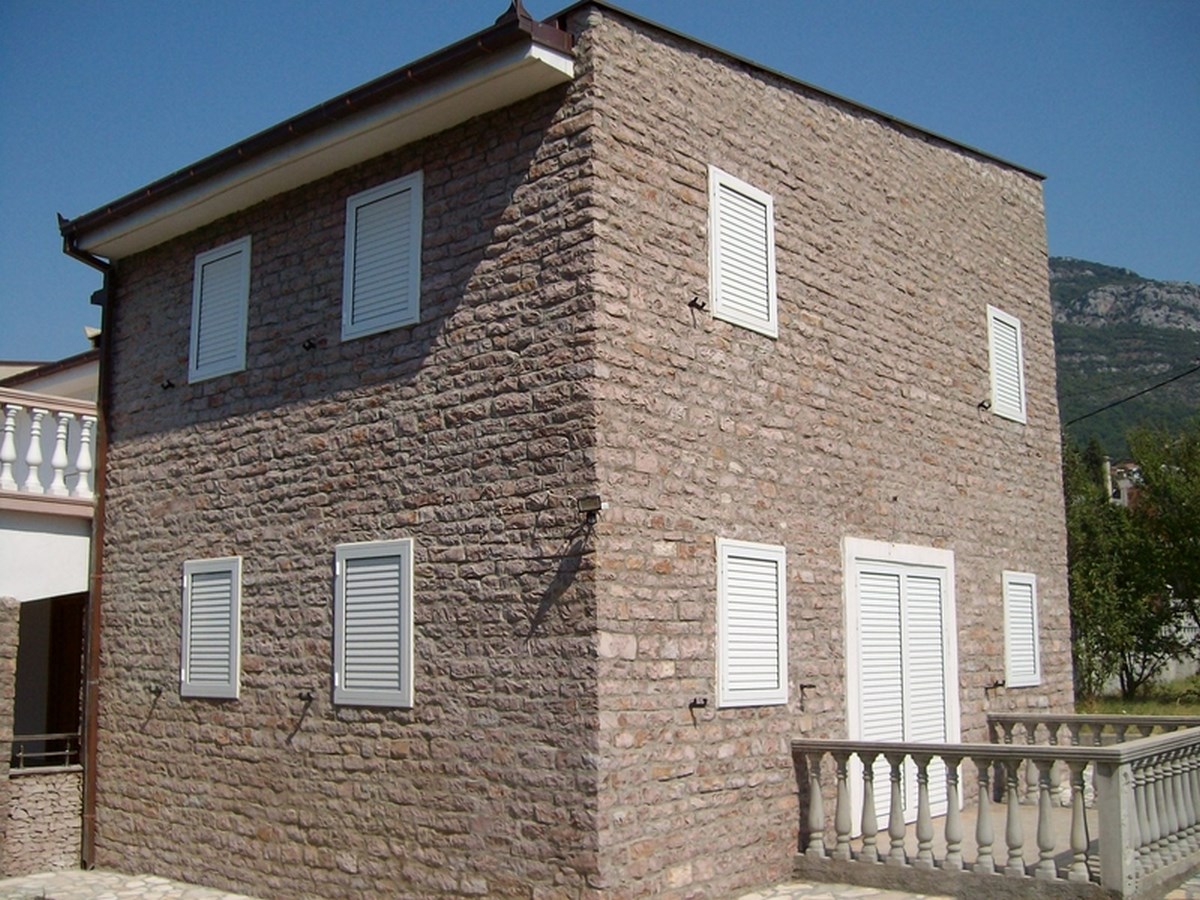 Two-story natural stone villa with white shutters in Bar, Montenegro. House facade with a terrace.