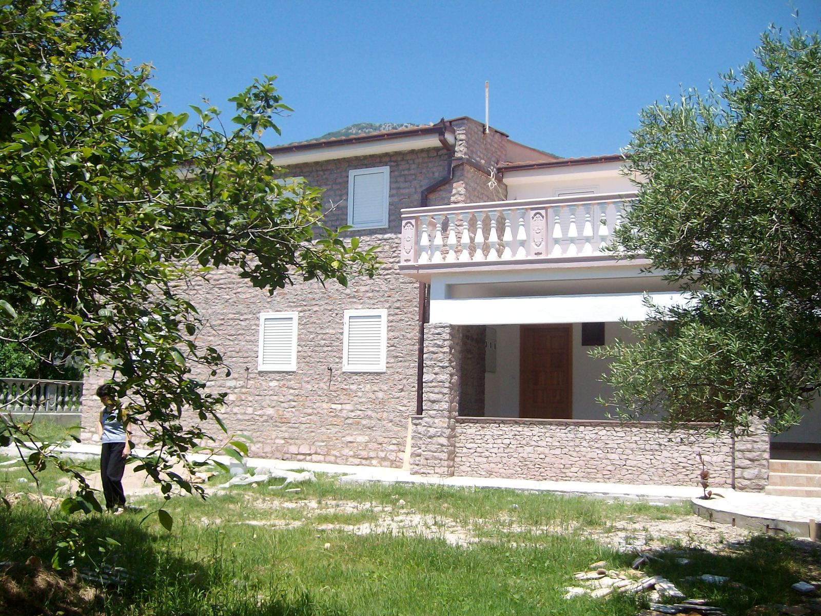 Two-story natural stone villa with a terrace and garden in Bar, Montenegro. House facade with white shutters.