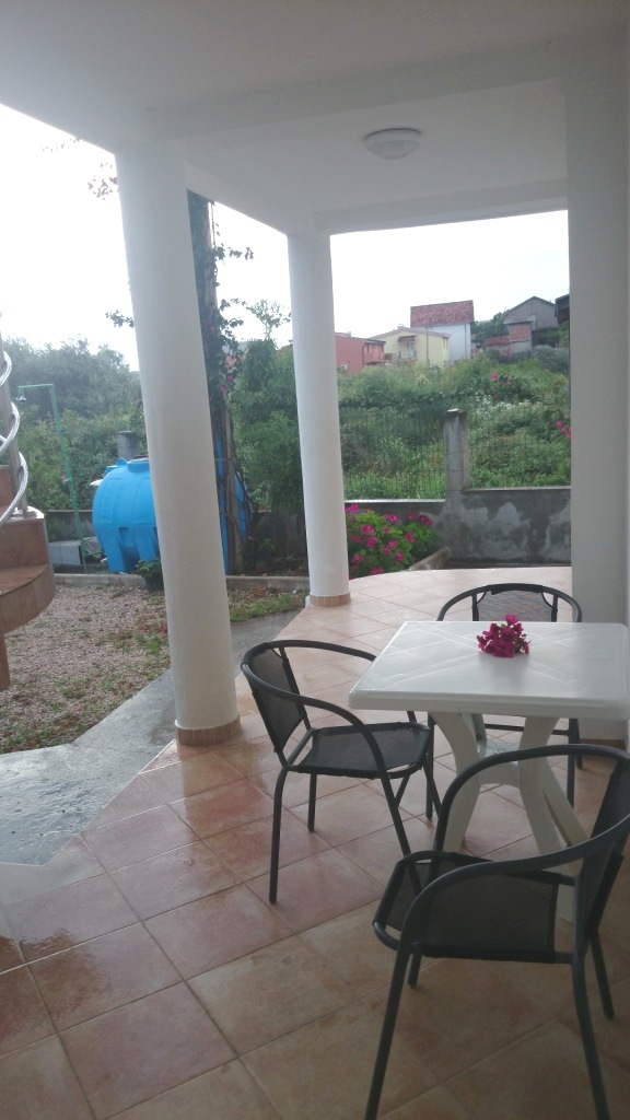 Covered terrace with white columns and garden furniture in a house, Shushan, Montenegro. View of a green garden and mountains.