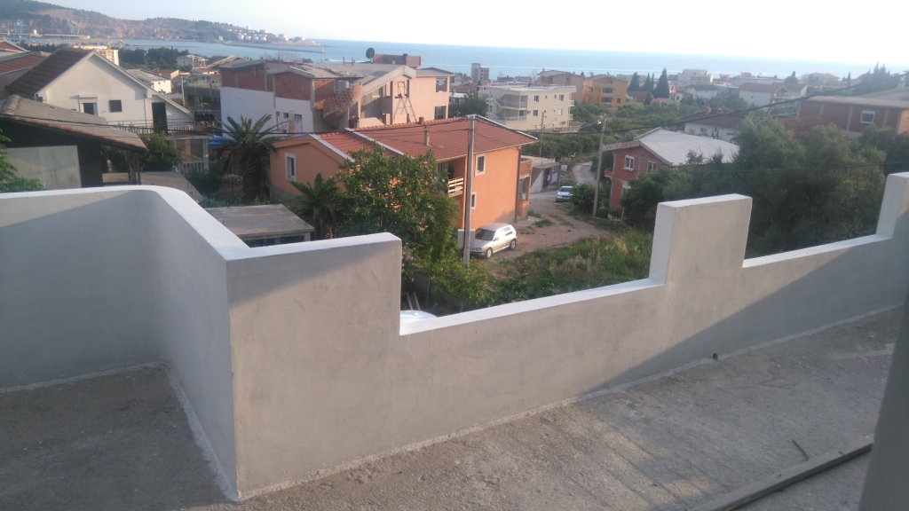 View from an open balcony in Shushan, Montenegro: a panorama of the sea, residential area, and mountains in clear weather.