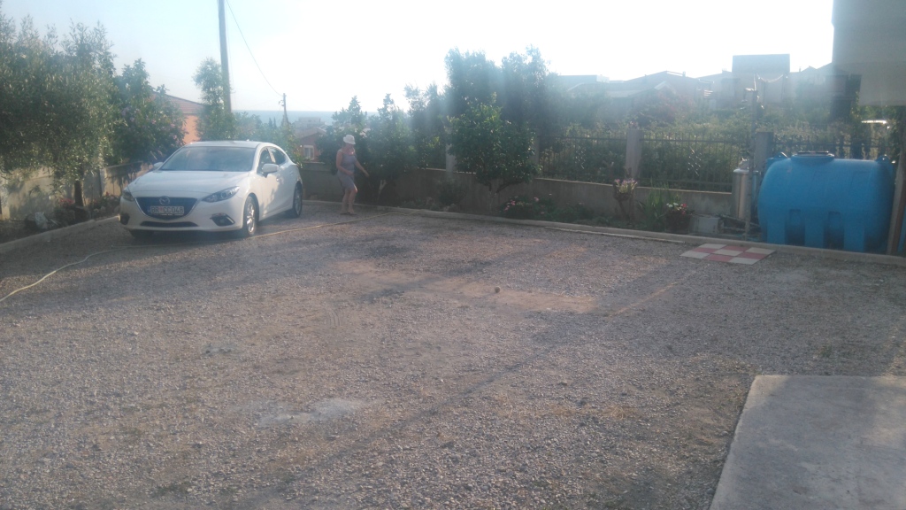 Private parking by the house in Shushan, Montenegro: gravel lot, car, and water tank on the property.